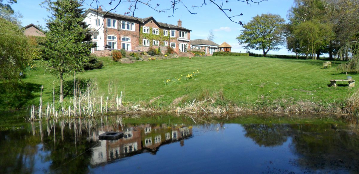 Image from next to lake looking up at large house with gazebo in garden